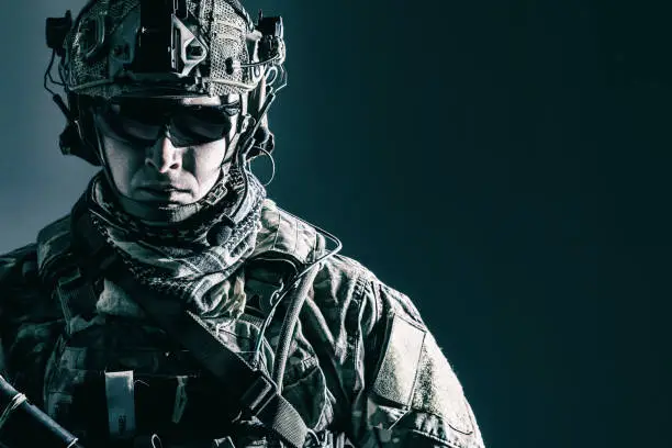 Elite member of US Army rangers in combat helmet and dark glasses. Studio shot, dark black background, looking at camera, dark contrast