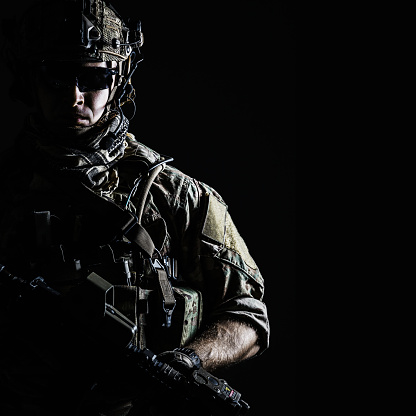 Elite member of US Army rangers in combat helmet and dark glasses. Studio shot, dark black background, looking at camera, dark contrast