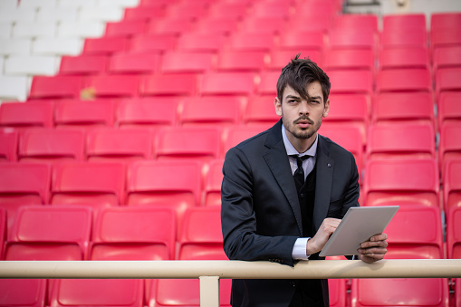 One man, young and handsome, soccer manager on the bleachers, using digital tablet.