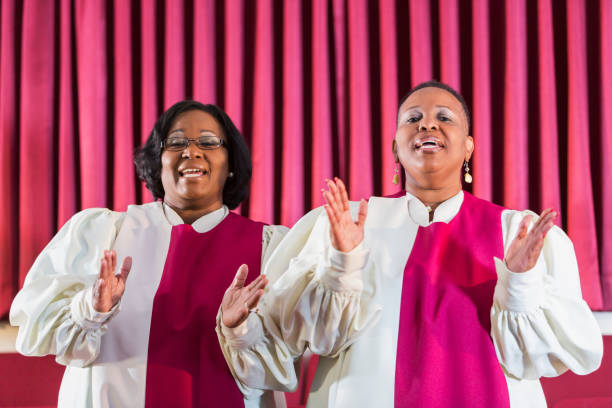 Two black women singing in church choir Two mature black women wearing robes, in a church choir. They are clapping, smiling at the camera. black female gospel singers stock pictures, royalty-free photos & images
