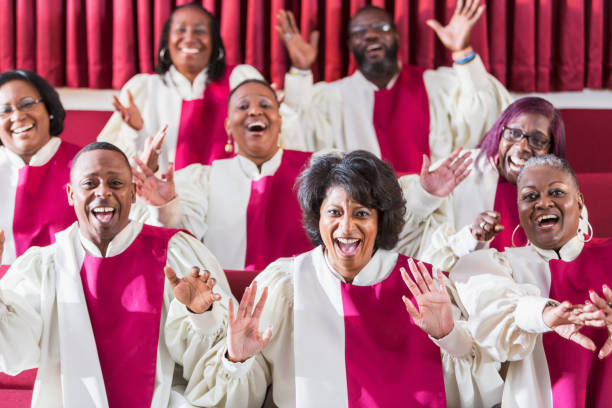 Mature black women and men singing in church choir A group of mature African American women and men wearing robes, singing in a church choir. gospel stock pictures, royalty-free photos & images