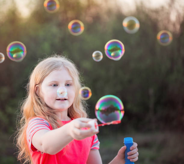istock girl blowing soap bubbles outdoor at sunset 690228178