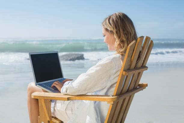 istock Gorgeous blonde sitting on deck chair using laptop on beach 690232714