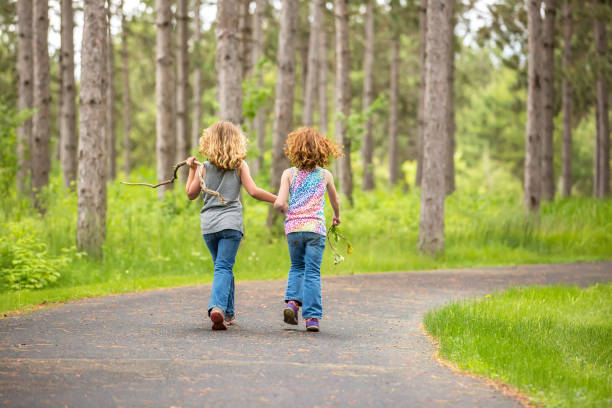 istock Two Young Girls Walking Through Woods on Paved Path 690251740