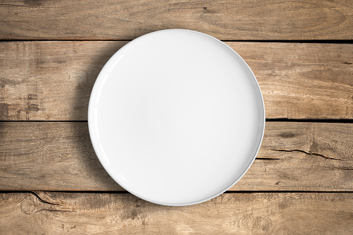 Top view of empty white food plate on a wood background.