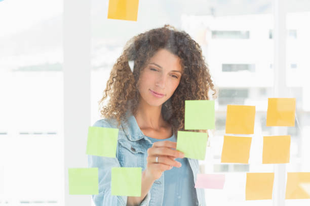 istock Smiling pretty designer looking at sticky notes on window 690259494