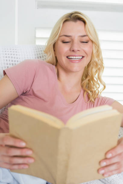 istock Happy blonde relaxing on the couch with book 690265694