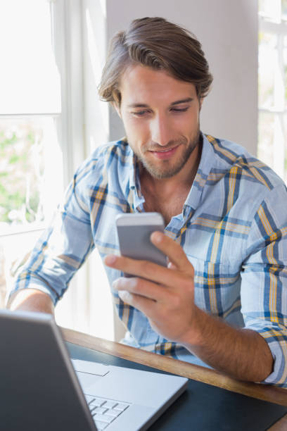 istock Smiling casual man using laptop and texting on smartphone 690265890