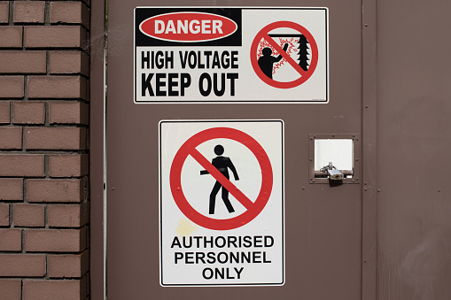 Metal sign with words, danger high voltage within keep out,attached to a wood door.