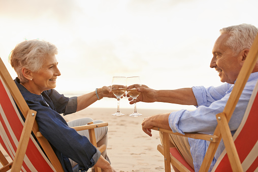 Shot of a senior couple relaxing on chairs and toasting with wine at the beach