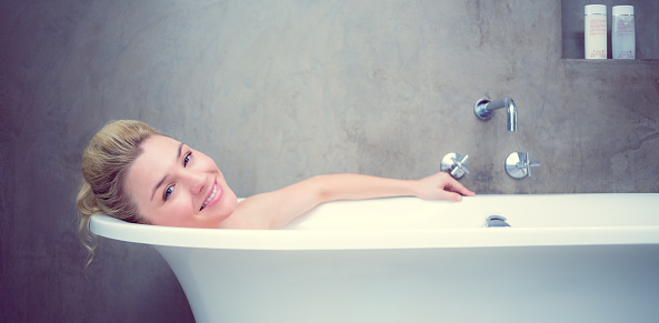 Serene blonde lying in the bath smiling at camera at home in the bathroom