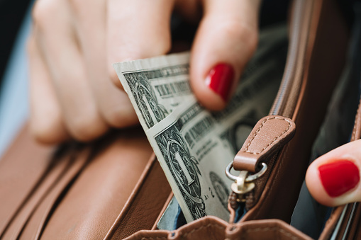 The girl's hand takes out paper dollars from a leather orange purse. Crisis and economy concept. Close-up.