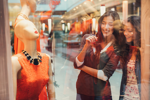 Two friends looking at a dress on mannequin in a clothing store.