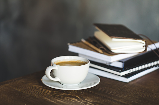 Close-up view of cup of coffee and notebooks on wooden table top