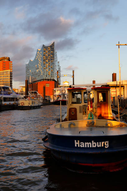 Hamburg, Germany - May 25, 2017: Sunset at Hamburg's historic harbor, with Elbphilharmonie concert hall (Elfi) in the centre and an old tugboat in front.