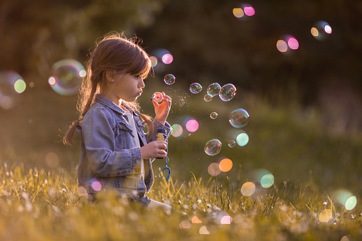 Small girl with bubble wand relaxing in the grass and blowing bubbles.