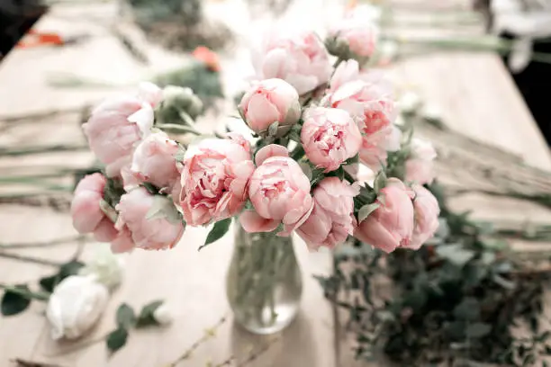 Pink peonies in vase on wooden floor and bokeh background - retro styled photo.