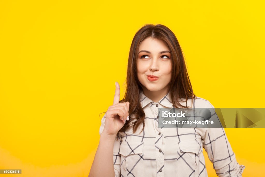 Thoughtful girl pointing up Pensive young girl thinking and pointing up on the yellow background. Looking Up Stock Photo