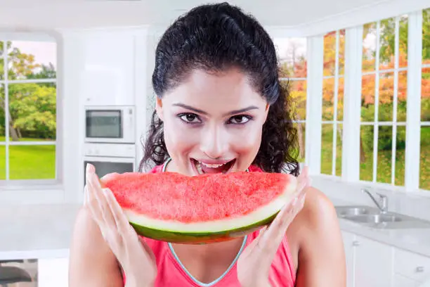 Greedy young woman eating a big slice of juicy watermelon with autumn background in the window