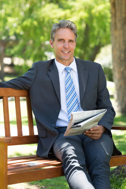 istock Businessman with newspaper sitting in park 690346958