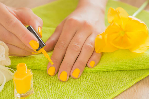 Hands cares about hands nails. Manicure beauty salon. Nail varnishing in yellow color. Spring and summer atmosphere with yellow and green colors. Hands cares about hands nails. Manicure beauty salon. Nail varnishing in yellow color. Spring and summer atmosphere with yellow and green colors. yellow nail polish stock pictures, royalty-free photos & images