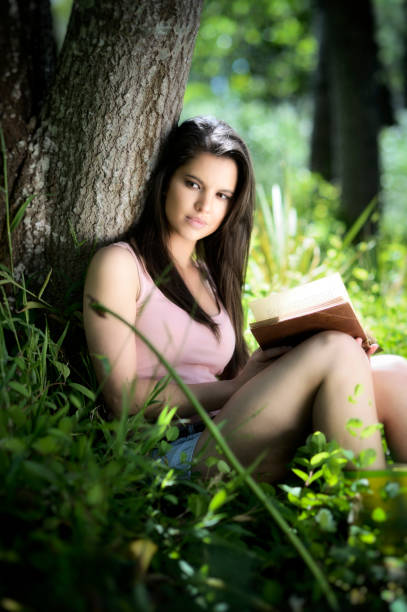 istock Young woman reads book in a forest 690369382