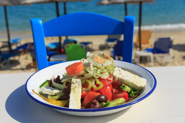 Griechischer Salat serviert am Meer, traditionellen griechischen Salat auf weißer Holztisch Hintergründe, Defocused Stuhl und Strand im Hintergrund – Foto