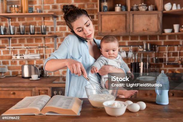 Mother Holding Her Son Talking On Smartphone And Mixing A Dough Stock Photo - Download Image Now