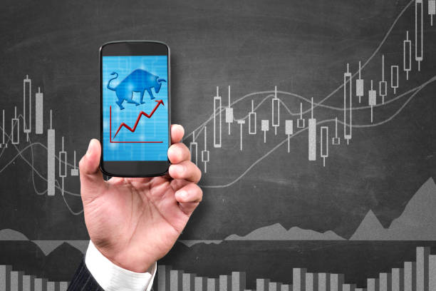 Bullish market Man holding smartphone with bulish trend indicating in blackboard in background stock market trading stock pictures, royalty-free photos & images