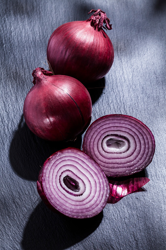 High angle view of three organic spanish onions on black slate table. One onion is half split. Predominant colors are purple and black. Low key DSRL studio photo taken with Canon EOS 5D Mk II and Canon EF 100mm f/2.8L Macro IS USM