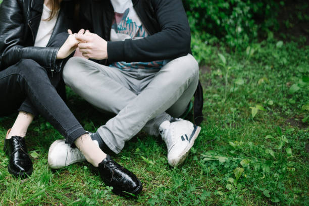 jambes de couple qu’assis dans le parc - human leg jeans converse shoe photos et images de collection