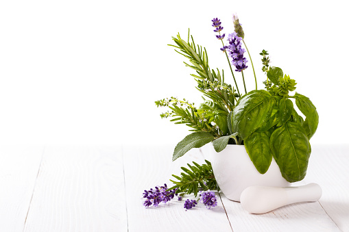 bunch of garden fresh herbs in a mortar over white isolated background