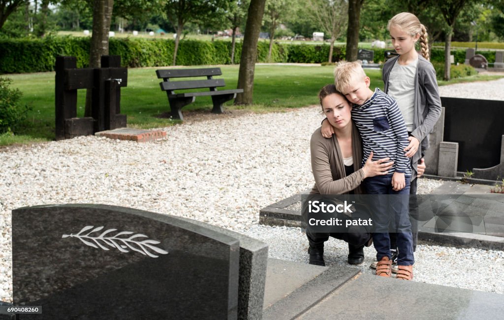 Young family visiting grave of family Young mother with kids visiting the grave at graveyard of deceased husband or grandparent Child Stock Photo