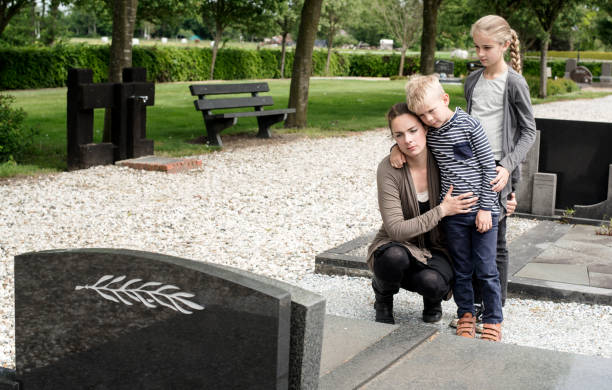 Young family visiting grave of family Young mother with kids visiting the grave at graveyard of deceased husband or grandparent sad child standing stock pictures, royalty-free photos & images