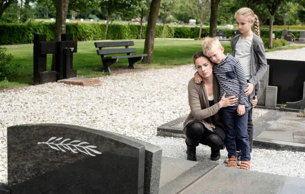 Young mother with kids visiting the grave at graveyard of deceased husband or grandparent