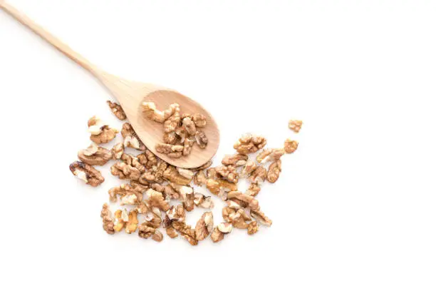 Peeled dried pieses of walnuts on wooden spoon isolated on white background