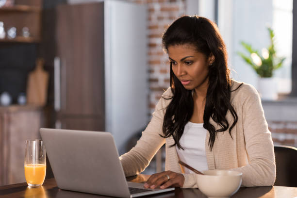 istock young african american woman having breakfast and using laptop at kitchen 690412314