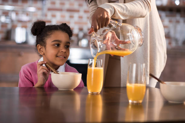 istock mother pouring juice into daughter's glass during breakfast at home 690414968
