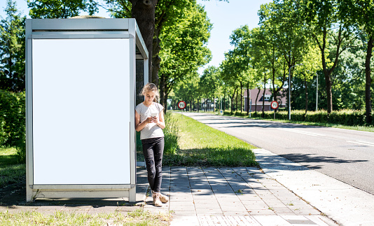 Bus stop advertising mockup with young girl using smartphone and waiting for the bus