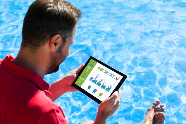 istock Man consulting web statistics with a tablet while sitting in the swimming pool edge. 690419970