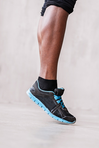Close up of legs of african young sportsman doing bouncing on toes. Focus on leg muscle and sneakers