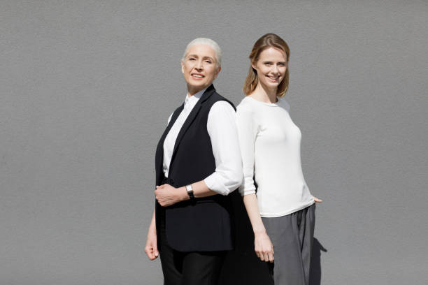 istock Two beautiful smiling women standing back ro back isolated on grey 690439876