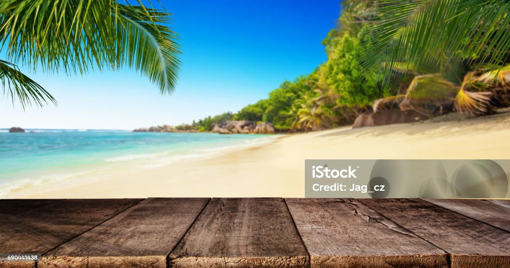 Tropical beach with wooden table, summer holiday background. Tropical beach with empty wooden table, summer holiday background. Travel and beach vacation, free space for text or product placement. Beach Stock Photo