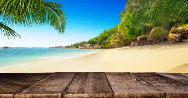 Tropical beach with empty wooden table, summer holiday background. Travel and beach vacation, free space for text or product placement.