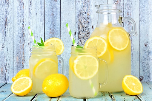 Vintage pitcher of lemonade with two mason jar glasses and lemons on rustic blue wood background