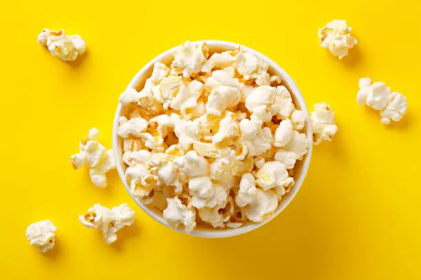 Photo of Popcorn viewed from above on yellow background. Flat lay of pop corn bowl. Top view