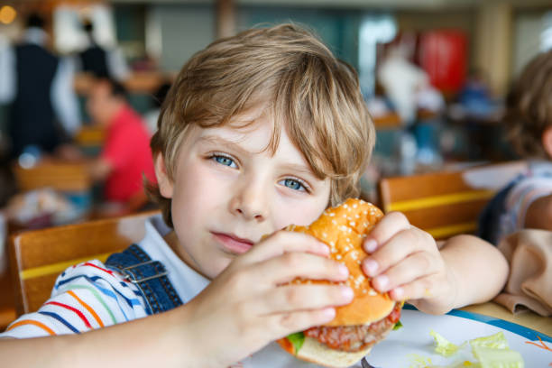 istock Cute healthy preschool boy eats hamburger sitting in school canteen 690514694