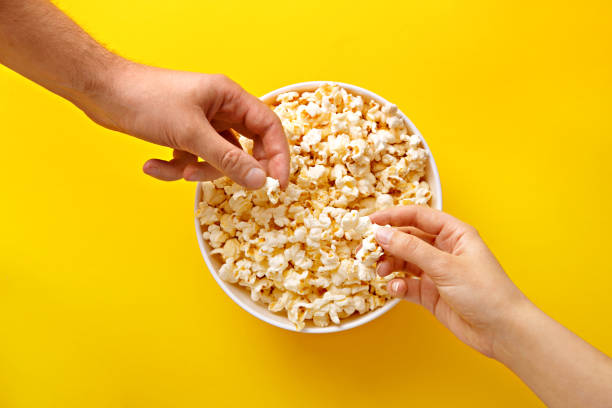 popcorn oglądany z góry na żółtym tle. ludzie jedzący popcorn. ludzkie ręce. widok z góry - popcorn snack bowl corn zdjęcia i obrazy z banku zdjęć