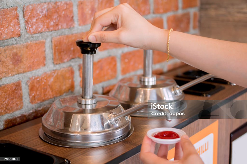 Woman's hand pumping the ketchup Woman's hand pumping the ketchup pump with brick wall pattern background Condiment Stock Photo