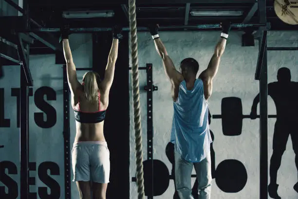 Young man and woman doing chin-ups together in gym.